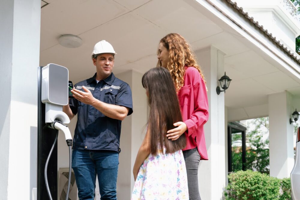 Technician install home EV charging station, providing service support for EV app on customer smartphone for monitoring charging status and set charging schedules at home.