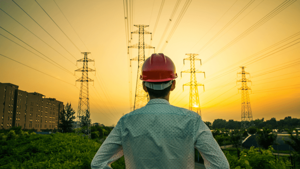 Man in a hard hard looking out at power lines